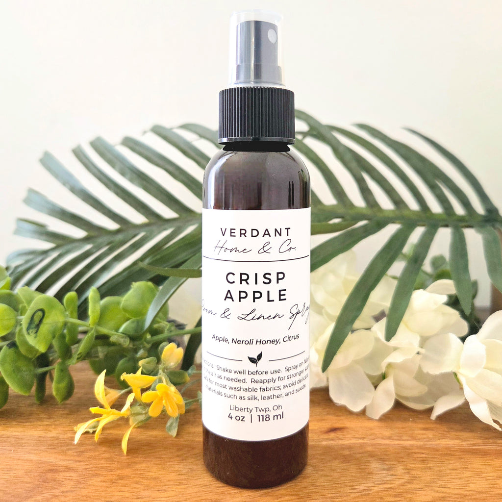 Bottle of Crisp Apple room & linen spray with greenery and flowers in the background