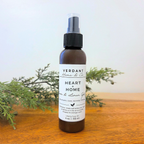 Bottle of Verdant Home & Co. 'Heart + Home' room spray on a wooden surface with greenery.