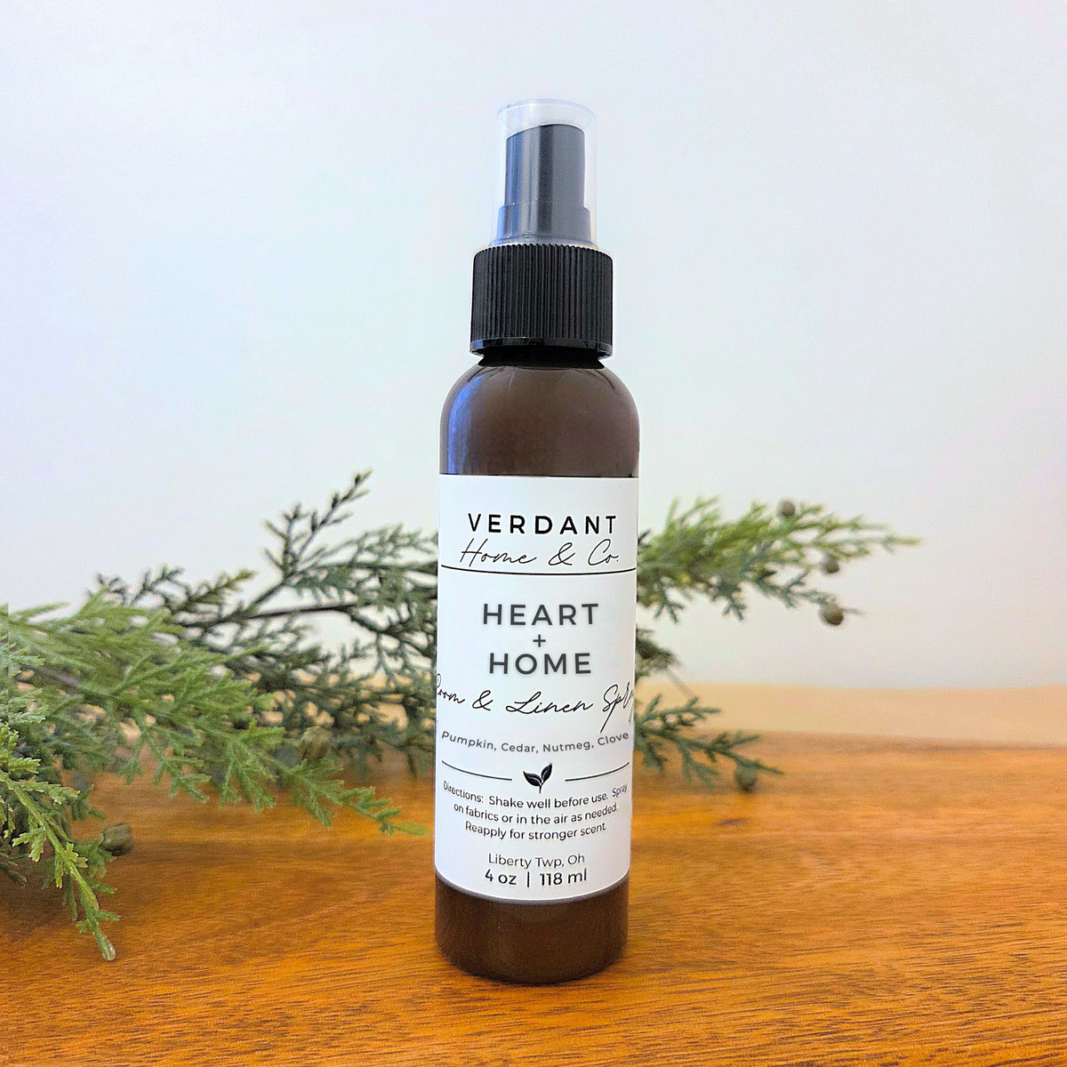 Bottle of Verdant Home & Co. 'Heart + Home' room spray on a wooden surface with greenery.