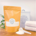 Yellow package of Verdant Home & Co laundry detergent with a scoop of powder on a wooden surface.