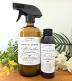 Two bottles of Verdant Home & Co Mango Crème Multi-Surface Cleaning Spray on a wooden surface with plants in the background.
