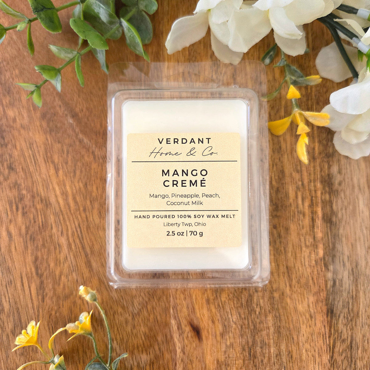 Verdant Home & Co. wax melt, Mango Creme, on a wooden surface with greenery and flowers.