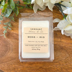 Verdant Home & Co. Moss + Iris wax melt on a wooden surface with flowers and greenery.