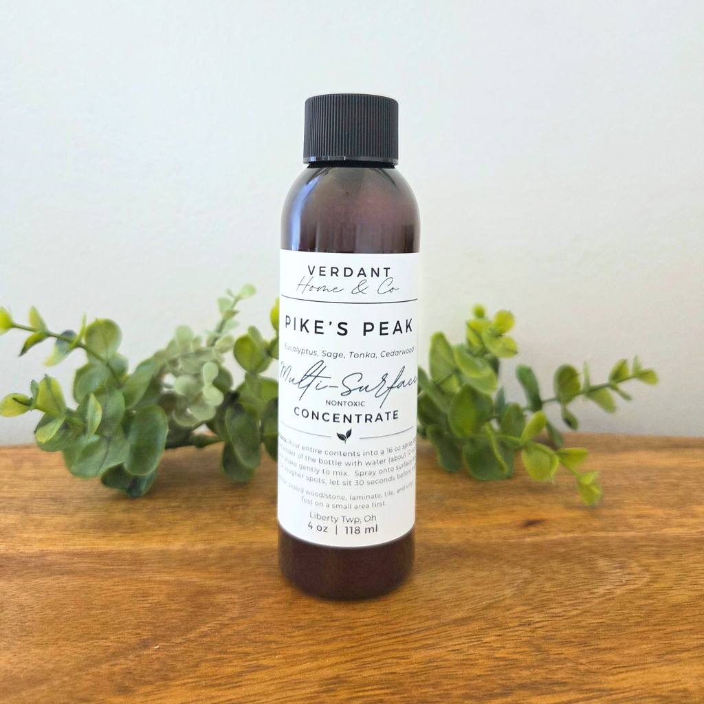 Bottle of Verdant Home & Co. product on a wooden surface with greenery in the background