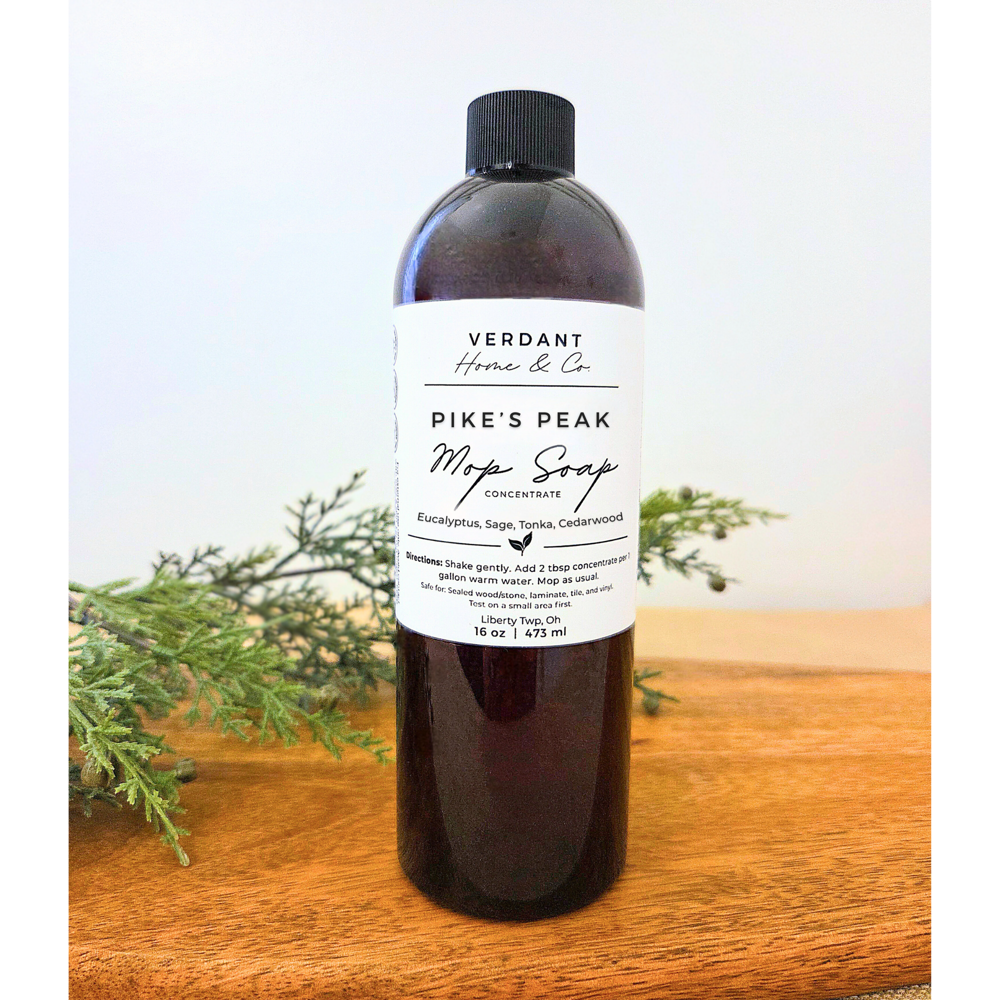 Bottle of Verdant Home & Co. Pike's Peak Mop Soap on a wooden surface with greenery in the background