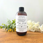 Bottle of Verdant Home & Co Pineapple Coconut Mop Soap on a wooden surface with flowers and greenery.