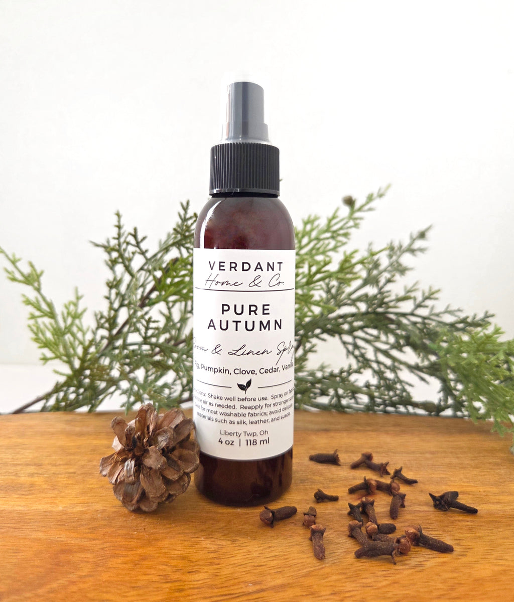 Brown bottle of Verdant Home & Co's room spray in the scent Pure Autumn, sitting on a wooden base with a pine cone and cloves sitting next to it.