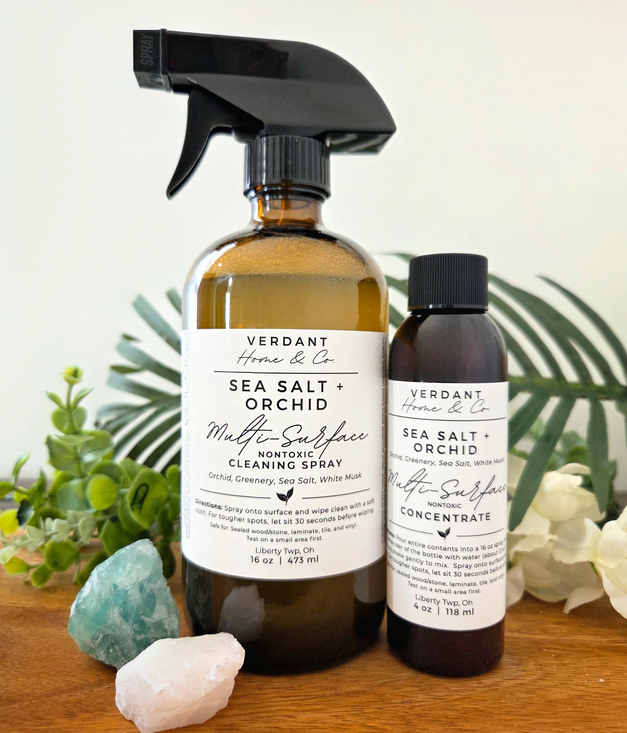 Two bottles of Verdant Home & Co Sea Salt + Orchid Multi-Surface Cleaner on a wooden surface with plants in the background.