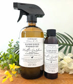 Two bottles of Verdant Home & Co. Sunkissed Paradise Multi-Surface Cleaning Spray and Concentrate on a wooden surface with plants in the background.