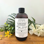 Bottle of Verdant Home & Co Sunkissed Paradise Mop Soap on a wooden surface with flowers and leaves.