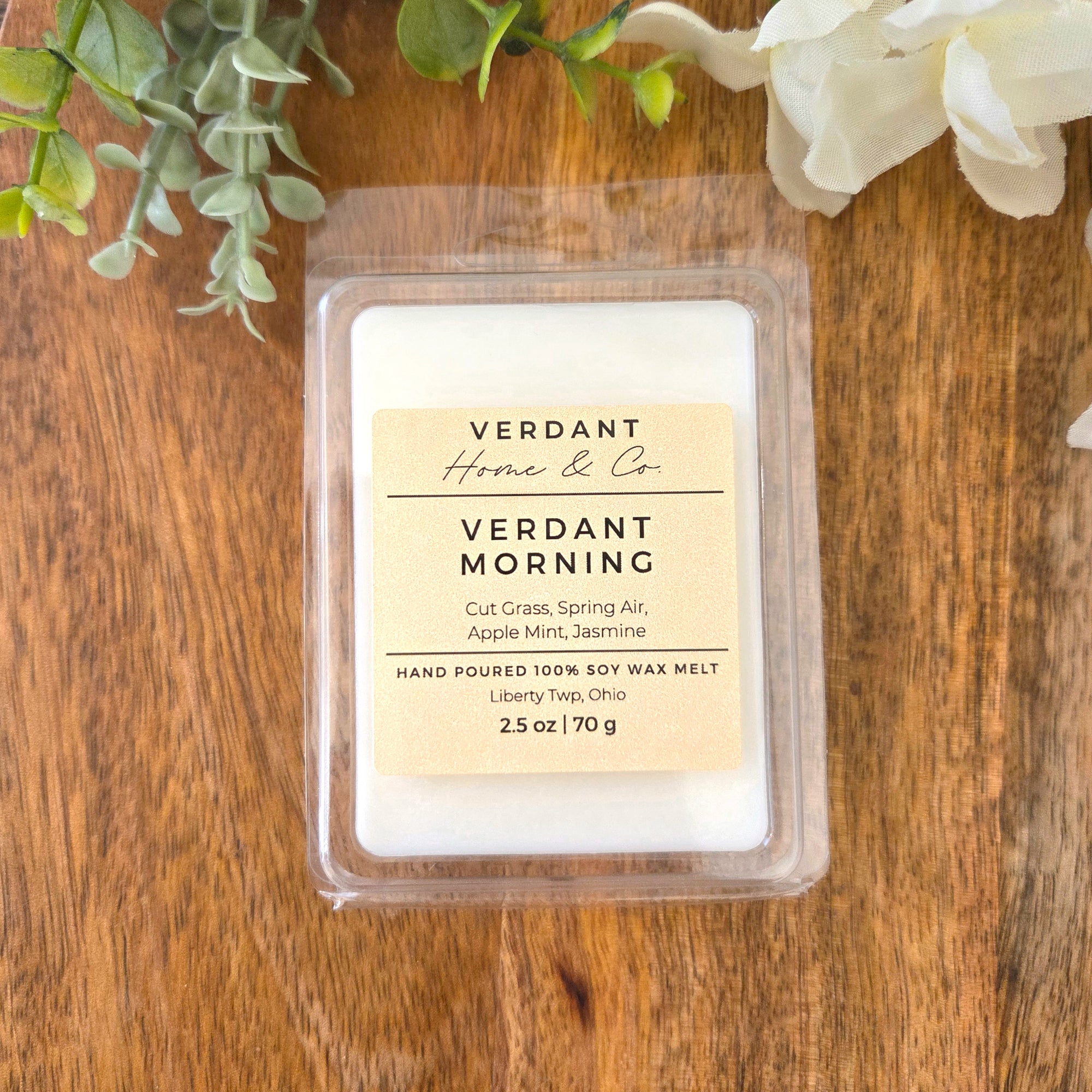 Verdant Home & Co. wax melt, Verdant Morning, on a wooden surface with greenery and flowers.