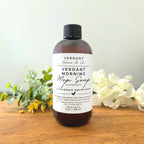 Bottle of Verdant Morning Mop Soap on a wooden surface with flowers and greenery.