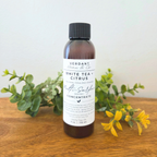 Bottle of Verdant Home & Co White Tea Citrus product on a wooden surface with greenery.