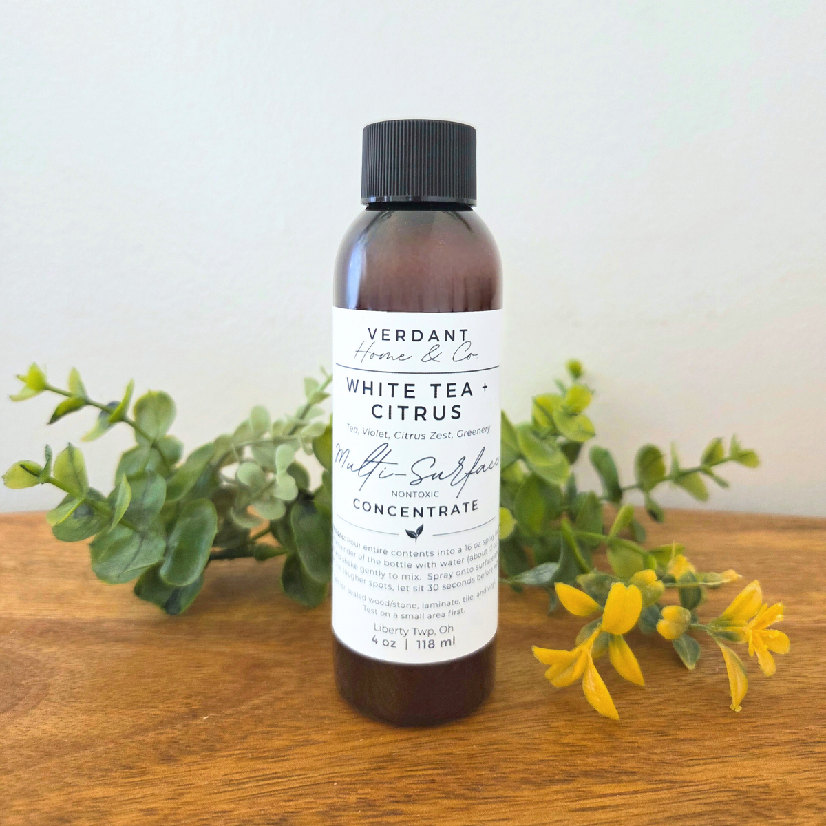 Bottle of Verdant Home & Co White Tea Citrus product on a wooden surface with greenery.