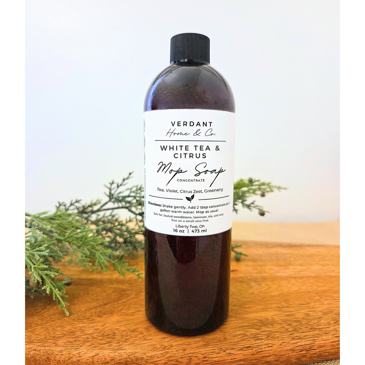 Bottle of Verdant Home & Co. White Tea & Citrus Mop Soap Concentrate on a wooden surface with greenery.