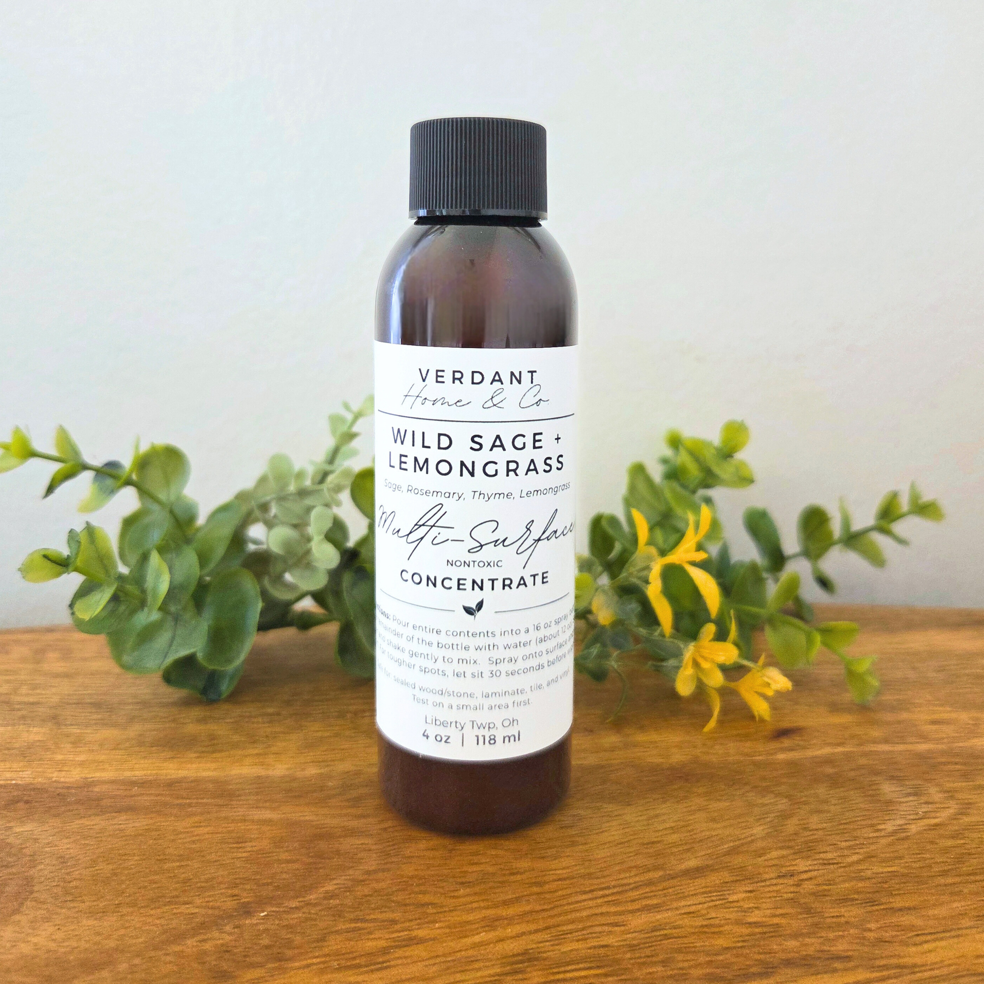 Bottle of Verdant Home & Co. Wild Sage & Lemongrass product on a wooden surface with greenery.