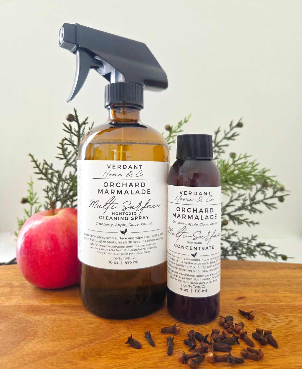 Two bottles of Verdant Home & Co Orchard Marmalade Multi-Surface Cleaning Spray on a wooden surface with plants in the background.