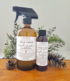 Two bottles of Verdant Home & Co Tree Farm Multi-Surface Cleaning Spray on a wooden surface with plants in the background.
